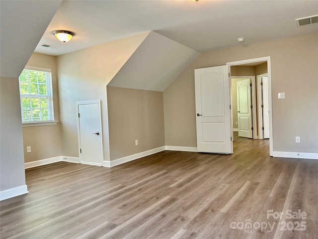 additional living space with baseboards, visible vents, wood finished floors, and lofted ceiling