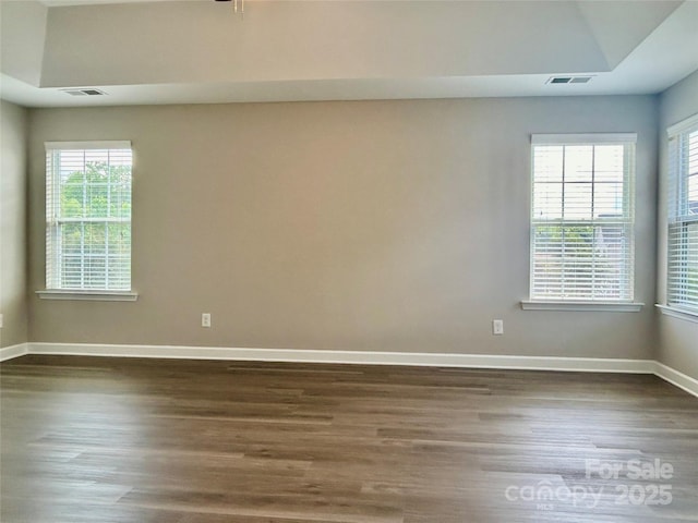 spare room featuring dark wood-style flooring, visible vents, and a wealth of natural light