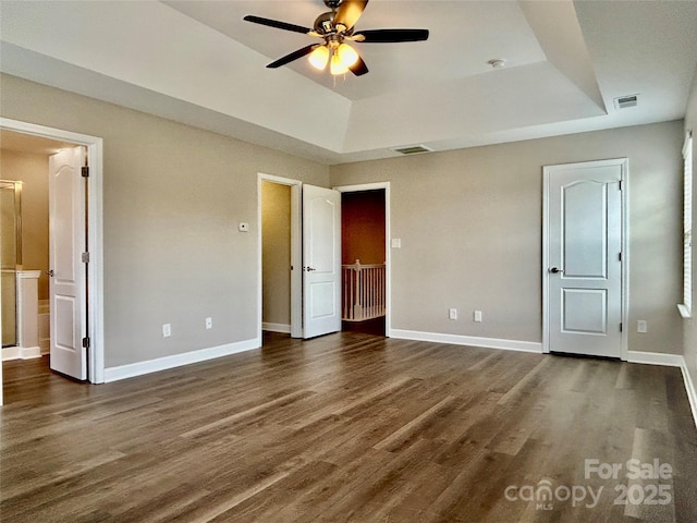 unfurnished bedroom featuring a tray ceiling, dark wood-type flooring, and visible vents