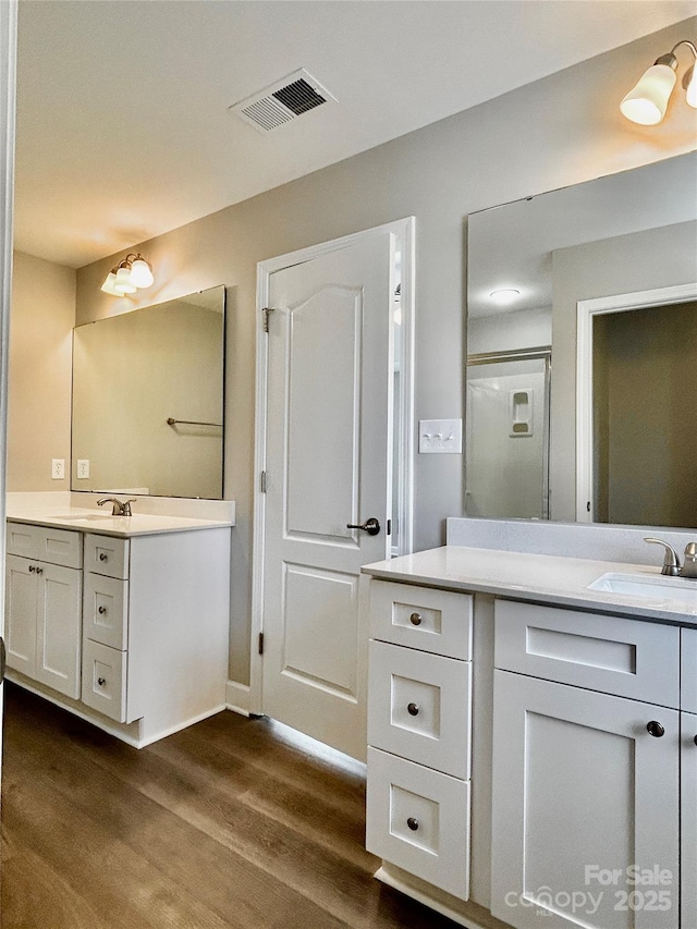 bathroom featuring a sink, two vanities, wood finished floors, visible vents, and a stall shower