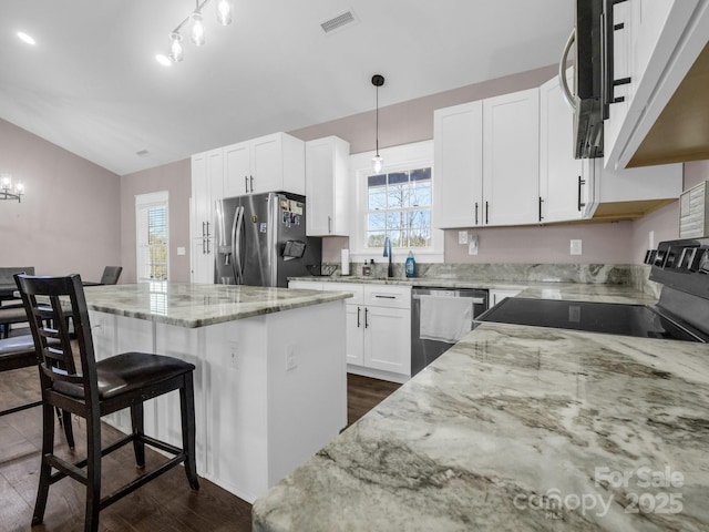 kitchen with light stone countertops, appliances with stainless steel finishes, a kitchen island, visible vents, and dark wood-style floors
