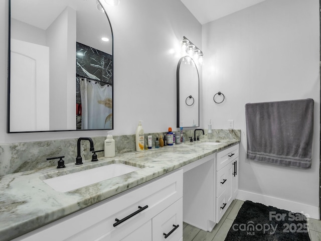 bathroom with a shower with shower curtain, double vanity, baseboards, and a sink