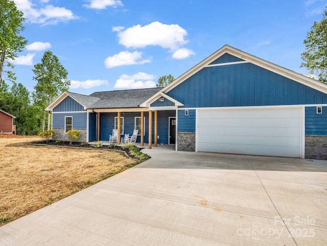 view of front of house with a porch, a front lawn, concrete driveway, an attached garage, and stone siding