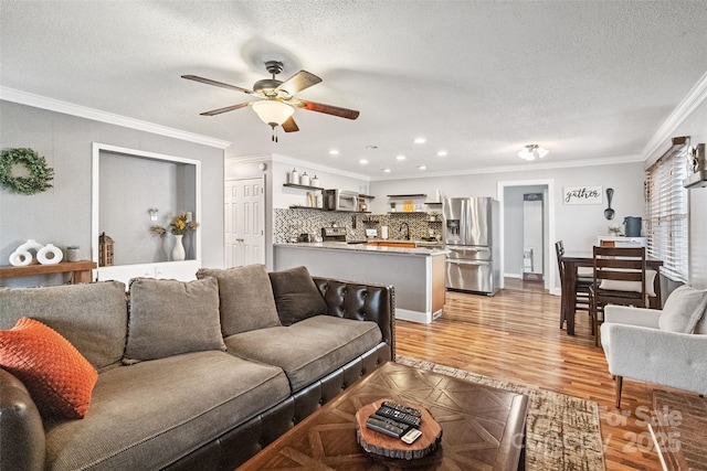 living room with a textured ceiling, ceiling fan, ornamental molding, and light wood finished floors