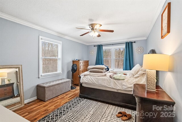 bedroom featuring visible vents, crown molding, baseboards, ceiling fan, and wood finished floors