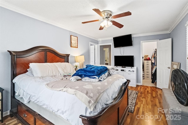 bedroom with a closet, crown molding, a ceiling fan, wood finished floors, and a walk in closet