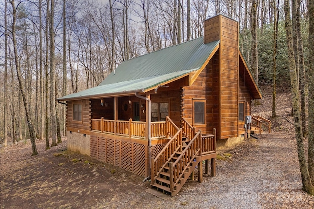 view of front of home with crawl space, covered porch, log siding, metal roof, and a chimney