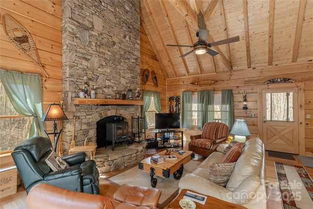 living room with wood walls, a wood stove, ceiling fan, and wood finished floors