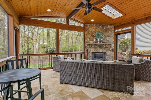 sunroom / solarium with beamed ceiling, an outdoor living space with a fireplace, a skylight, and a ceiling fan