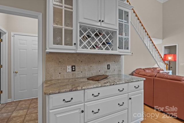 kitchen with glass insert cabinets, white cabinetry, light stone countertops, and tasteful backsplash