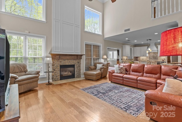 living area featuring crown molding, a fireplace, light wood-style flooring, visible vents, and ceiling fan