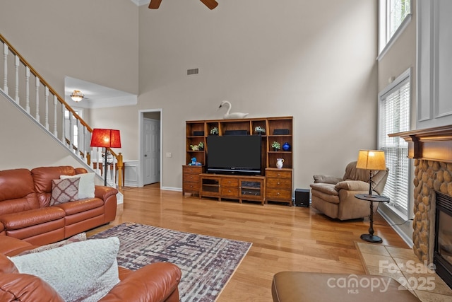 living room featuring stairs, light wood-style floors, visible vents, a ceiling fan, and a fireplace