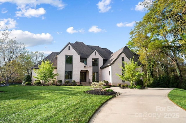 french provincial home with driveway, a shingled roof, and a front lawn