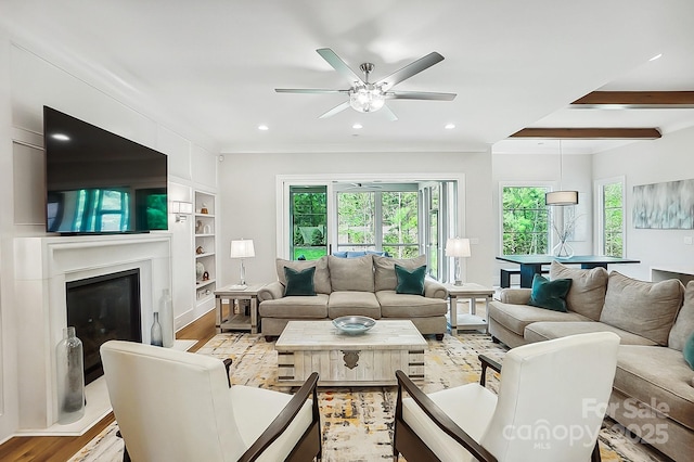 living room featuring a glass covered fireplace, recessed lighting, ceiling fan, light wood-style flooring, and built in features