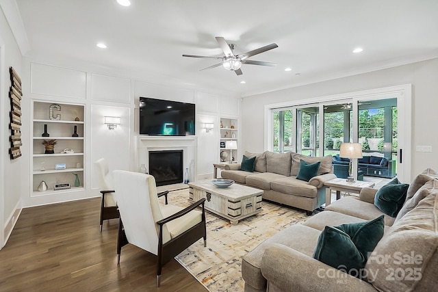 living room with wood finished floors, ornamental molding, and built in shelves