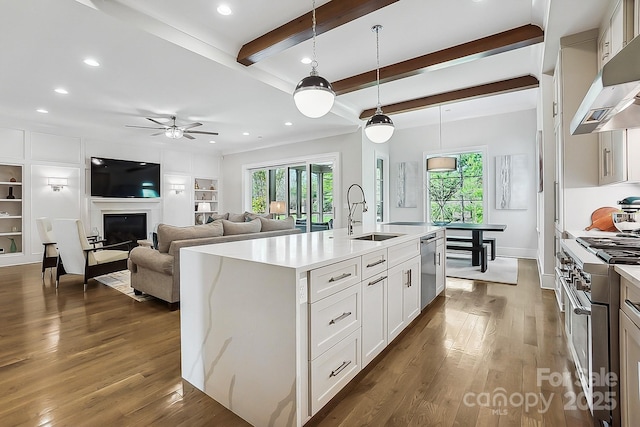 kitchen featuring beamed ceiling, wood finished floors, wall chimney exhaust hood, appliances with stainless steel finishes, and a sink