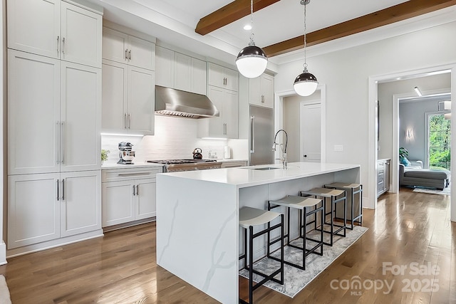 kitchen with stainless steel built in refrigerator, a sink, a center island with sink, light wood-type flooring, and exhaust hood