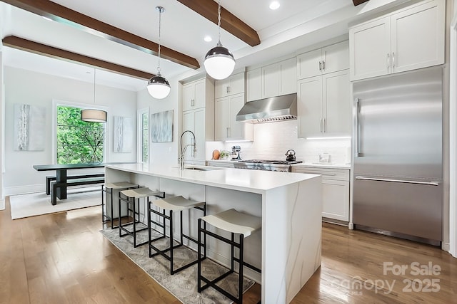 kitchen featuring a sink, range hood, wood finished floors, built in fridge, and decorative backsplash