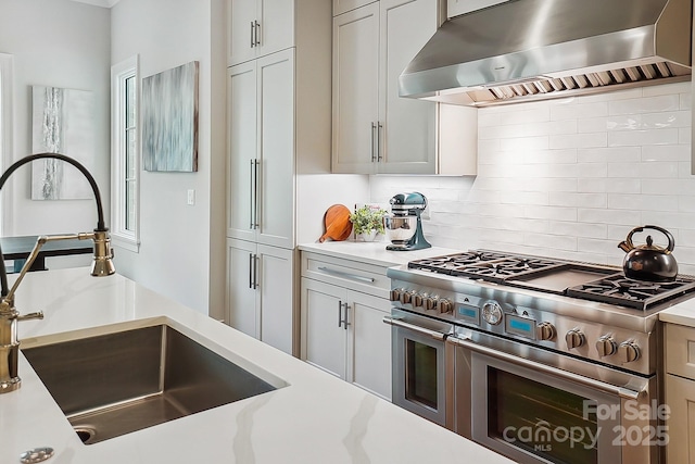 kitchen featuring double oven range, backsplash, wall chimney exhaust hood, and a sink