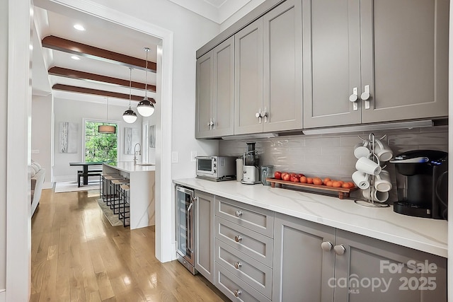 kitchen featuring wine cooler, gray cabinetry, decorative backsplash, beam ceiling, and light wood-style floors