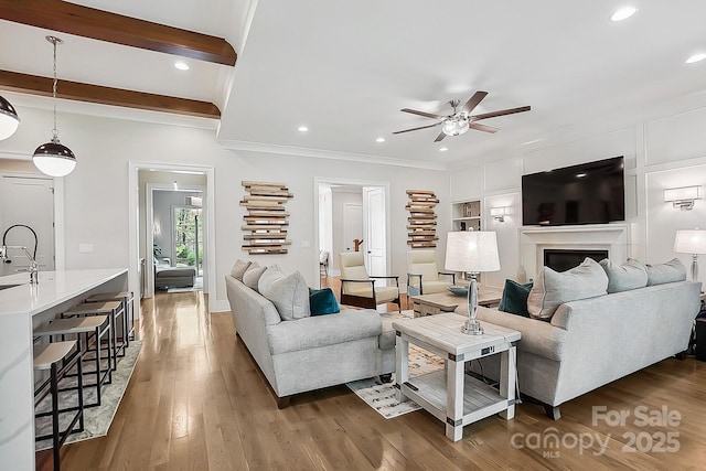 living area with beamed ceiling, ornamental molding, wood finished floors, a ceiling fan, and built in features