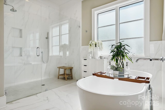 full bathroom featuring marble finish floor, a wealth of natural light, a stall shower, and tile walls