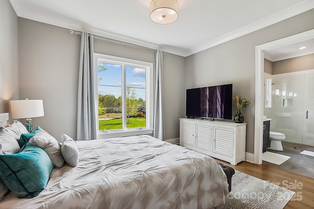 bedroom featuring baseboards, crown molding, wood finished floors, and ensuite bath