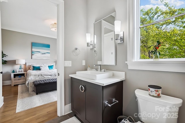 ensuite bathroom featuring baseboards, wood finished floors, toilet, vanity, and ensuite bath