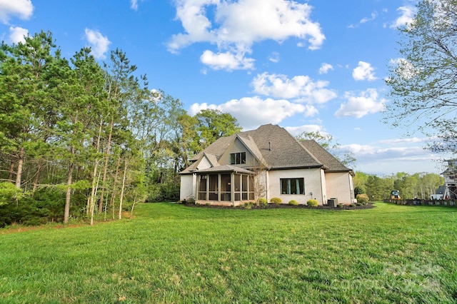 rear view of property featuring roof with shingles, a sunroom, central AC, and a yard