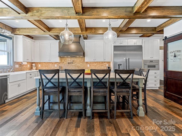 kitchen featuring a kitchen island with sink, appliances with stainless steel finishes, premium range hood, white cabinets, and coffered ceiling