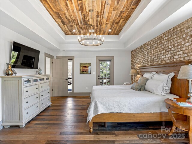 bedroom with access to outside, an inviting chandelier, a raised ceiling, baseboards, and dark wood-type flooring