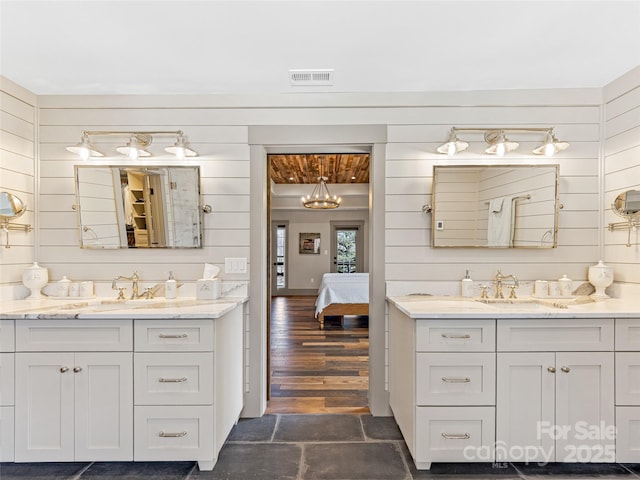 ensuite bathroom with a sink, wooden walls, and two vanities
