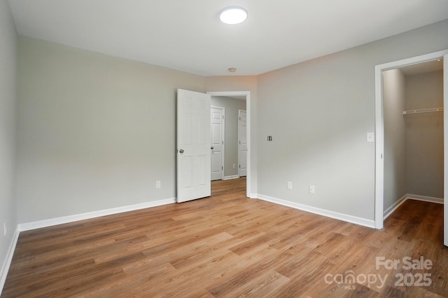 unfurnished bedroom featuring a closet, a spacious closet, light wood-style floors, and baseboards