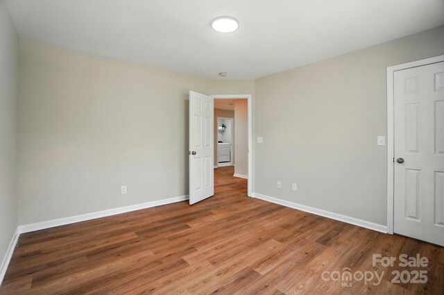unfurnished bedroom featuring washer / clothes dryer, baseboards, and wood finished floors