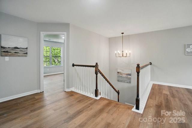 stairway featuring baseboards, a chandelier, and wood finished floors