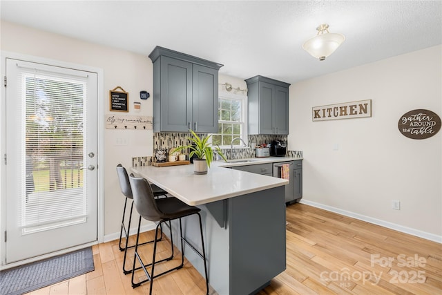 kitchen featuring light countertops, a sink, a breakfast bar, a peninsula, and light wood-style floors