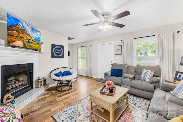 living area featuring a tiled fireplace, wood finished floors, a textured ceiling, baseboards, and ceiling fan