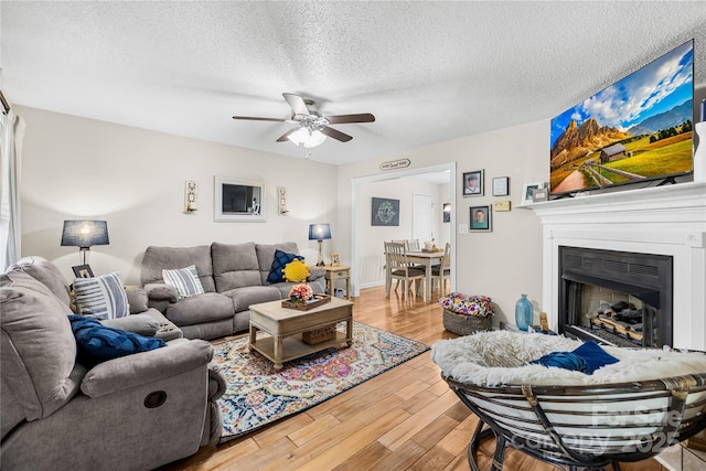 living room with a textured ceiling, a fireplace, wood finished floors, and a ceiling fan