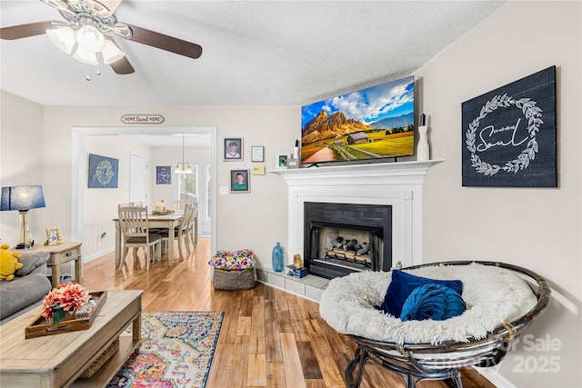 living room with a fireplace, a textured ceiling, wood-type flooring, baseboards, and ceiling fan