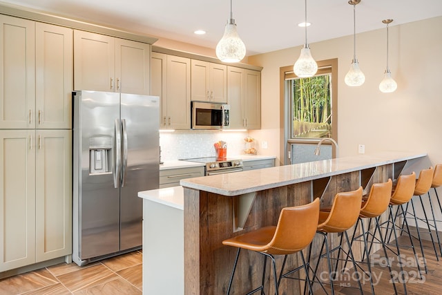 kitchen with a kitchen bar, a peninsula, appliances with stainless steel finishes, hanging light fixtures, and backsplash