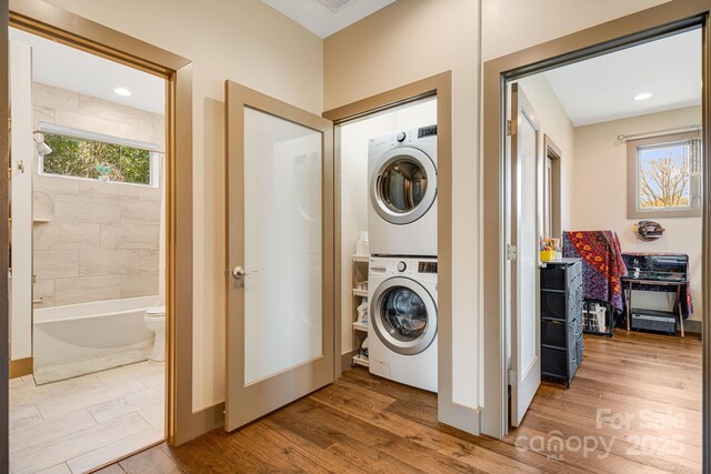 laundry room featuring stacked washer / dryer, wood finished floors, and plenty of natural light
