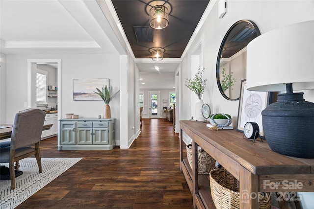corridor with crown molding, a raised ceiling, dark wood finished floors, baseboards, and visible vents