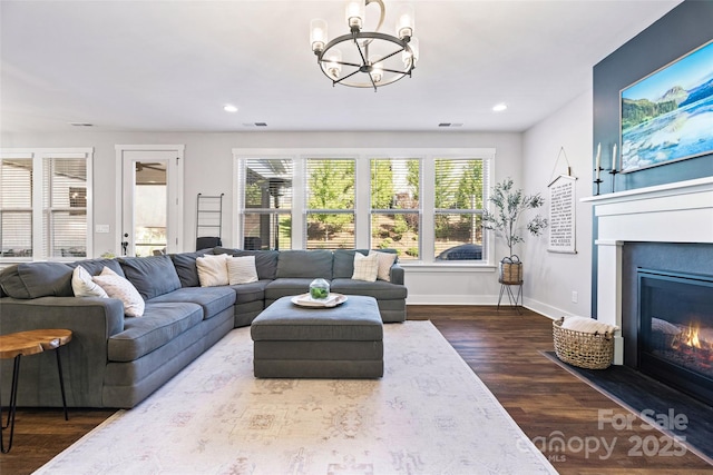 living area with an inviting chandelier, dark wood-style flooring, a glass covered fireplace, and recessed lighting