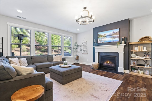 living room with visible vents, wood finished floors, a glass covered fireplace, and a chandelier