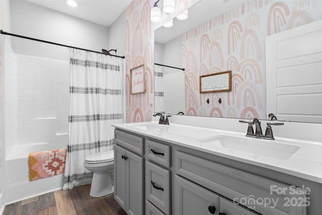full bathroom with wallpapered walls, a sink, toilet, and wood finished floors