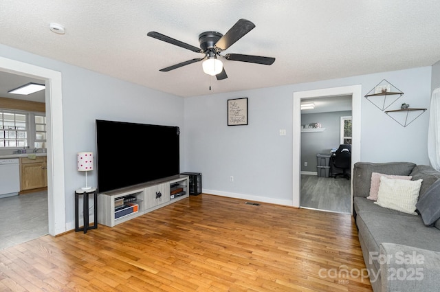 living area featuring a textured ceiling, light wood-type flooring, visible vents, and a ceiling fan