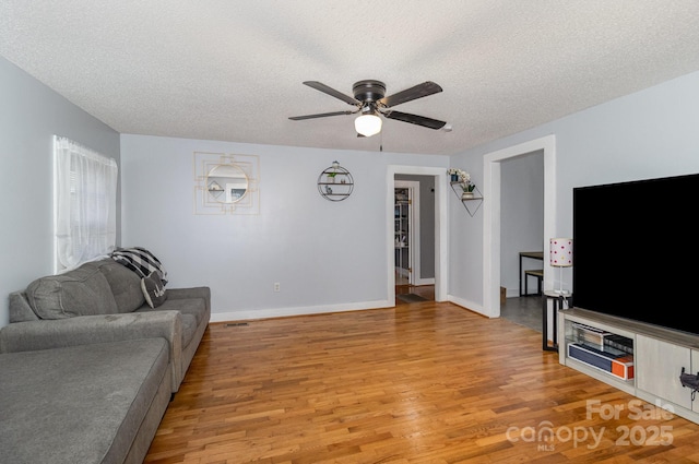 living area featuring baseboards, a textured ceiling, light wood-style floors, and a ceiling fan