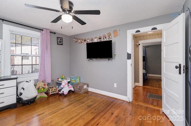 playroom with a ceiling fan, a textured ceiling, baseboards, and wood finished floors