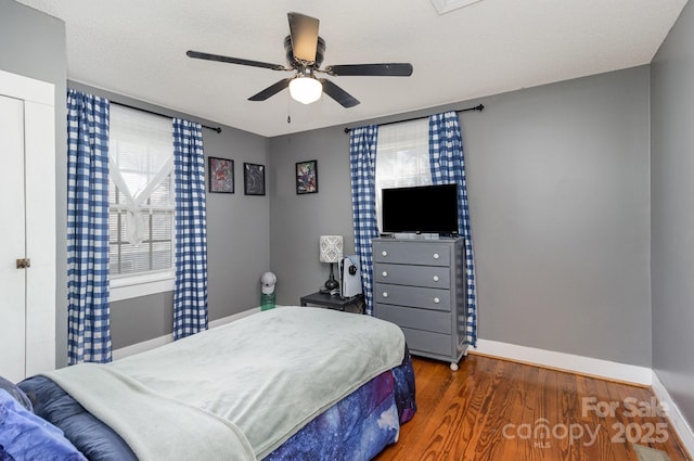 bedroom with a textured ceiling, baseboards, wood finished floors, and a ceiling fan