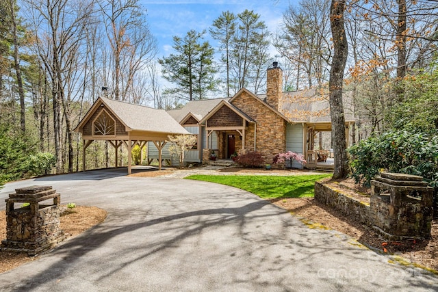 view of front of house with driveway, a chimney, roof with shingles, a carport, and stone siding